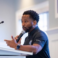 Man looks at GVSU Alumni crowd with microphone in hand at the podium